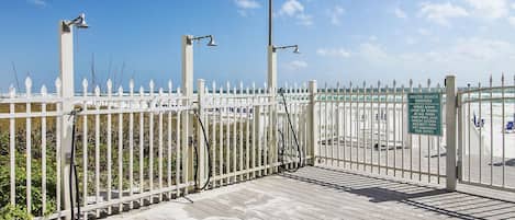 Une jetée en bois, agrémentée d’une clôture blanche, de lampadaires en métal et d’un panneau indiquant les conditions d’accès à la plage.