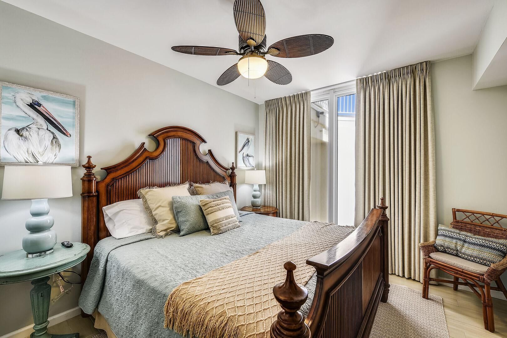 Une chambre à coucher avec un lit en bois, un ventilateur de plafond, une table de chevet, une chaise et une fenêtre avec des rideaux.