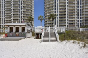 Ein Strandhotel mit einer Stranddusche, einer Treppe, die zu einem Balkon führt, und einer Palme.