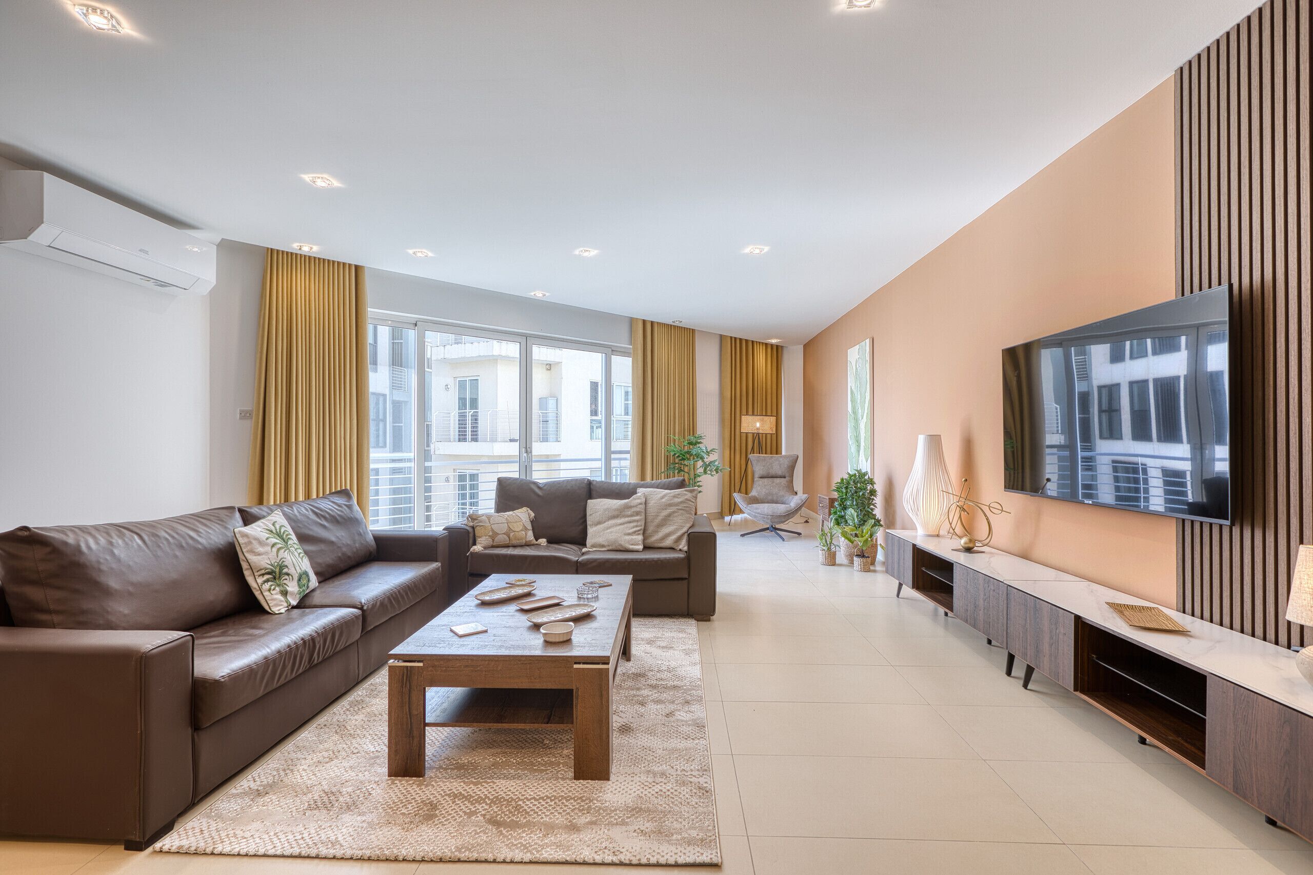 Un salon moderne avec un canapé, une table basse, un téléviseur et une grande fenêtre.