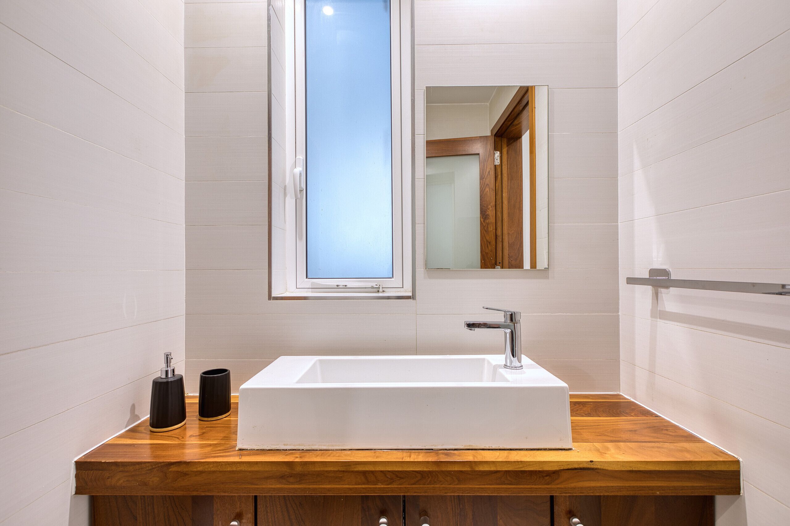 Ein Badezimmer mit einem Holzkosmetikschrank, einem weißen Waschbecken, einem Spiegel und einem Fenster.