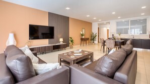 Ein modernes Wohnzimmer mit Sofa, Fernseher, Essbereich und Küche.