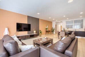 Ein modernes Wohnzimmer mit Sofa, Fernseher, Essbereich und Küche.