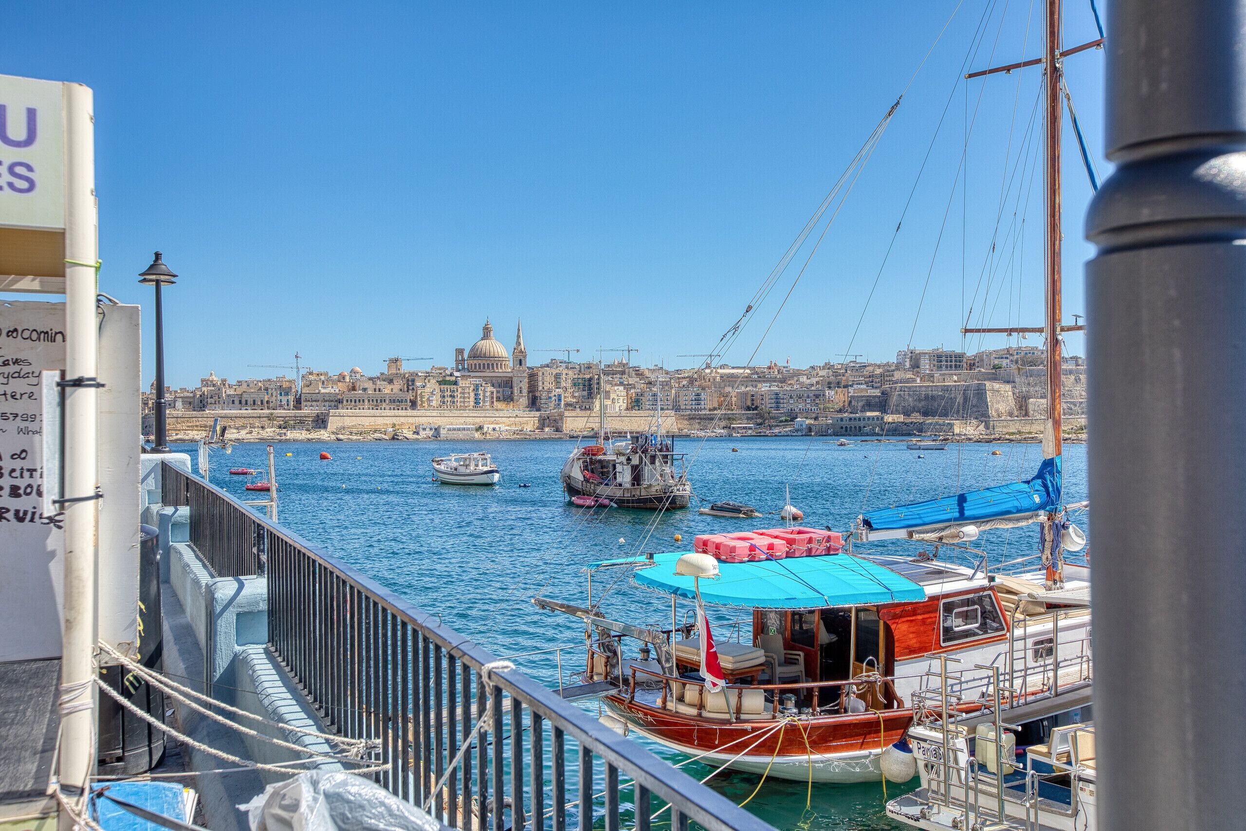 A harbor with boats, a city skyline in the background, and a clear blue sky.