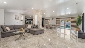 Uma sala de estar moderna com um sofá em seção, uma mesa de centro de vidro e uma área de jantar com vista para a piscina.