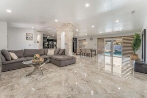 Ein modernes Wohnzimmer mit einer Eckcouch, einem Glastisch und einem Essbereich mit Blick auf einen Pool.