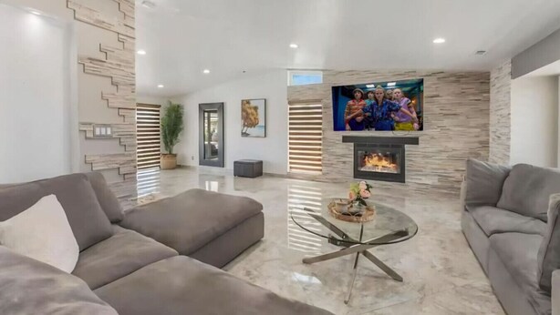 Uma sala de estar moderna com dois sofás, uma mesa de centro de vidro, uma lareira e uma TV fixada na parede.