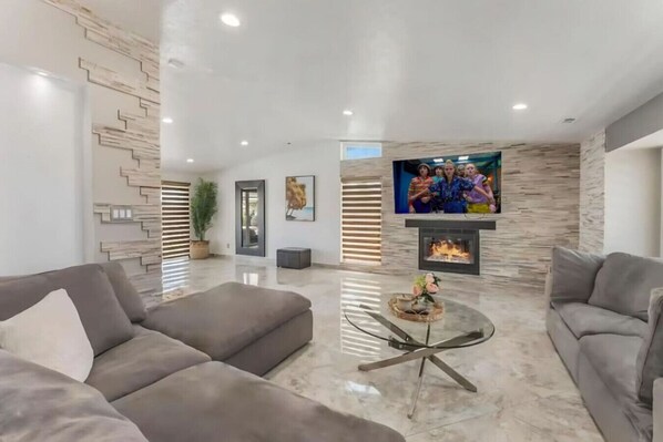 Ein modernes Wohnzimmer mit zwei Sofas, einem Glastisch, einem Kamin und einem an der Wand befestigten Fernseher.