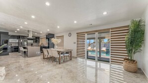 Uma sala de estar ampla com mesa de jantar, cadeiras, cozinha e vista para uma piscina.