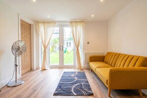 A room with a sofa, a standing fan, a patterned rug, and a view through a glass door.