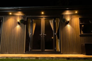 A building with a large glass door, vertical wooden siding, and two wall-mounted lights.