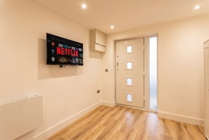 Habitación con una televisión de pantalla plana montada en la pared mostrando contenido de Netflix, una puerta con paneles de vidrio esmerilado y suelo de madera.