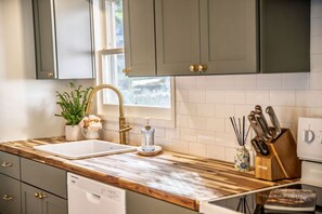 A kitchen with a wooden countertop, a double sink, a potted plant, a knife block, and a dishwasher. - Stylish Waterfront Retreat in Bayview-Boat Dock (Bayview)