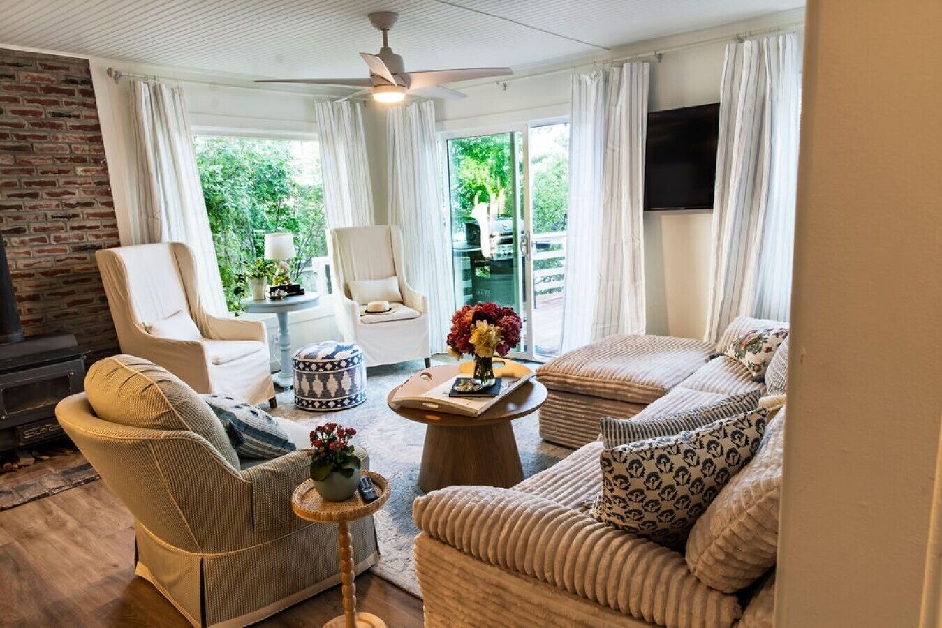 A cozy living room with a fireplace, comfortable seating, and a large window offering a view of greenery.