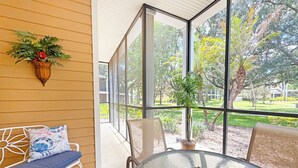 Ein Zimmer mit Glastisch, einer Bank mit Kissen, einer Topfpflanze und Blick auf einen Garten durch große Fenster.