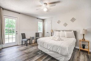 A bedroom with a bed, a ceiling fan, two chairs, a nightstand with a lamp, and a window with curtains. - Fenced Yard, Centrally Located-Parkway Village Pad (Memphis)