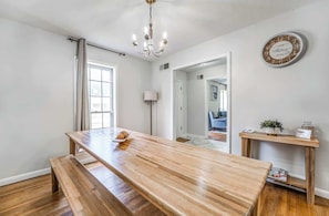 A spacious room with a wooden dining table, bench, chandelier, and a clock on the wall. - Fenced Yard, Centrally Located-Parkway Village Pad (Memphis)