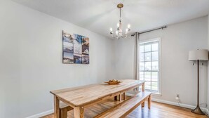 Habitació amb taula de dinar de fusta, una banca, un candelabrum, obra d'art a la paret i una finestra amb cortines.