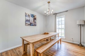 A room with a wooden dining table, bench, chandelier, artwork on the wall, and a window with curtains. - Fenced Yard, Centrally Located-Parkway Village Pad (Memphis)