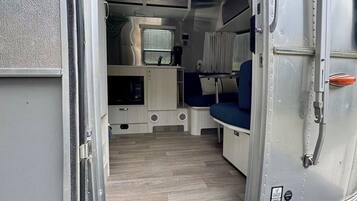 An open van with a kitchen area, a sleeping berth, and a door mat with 'Adventure Inspired by Airstream' text.