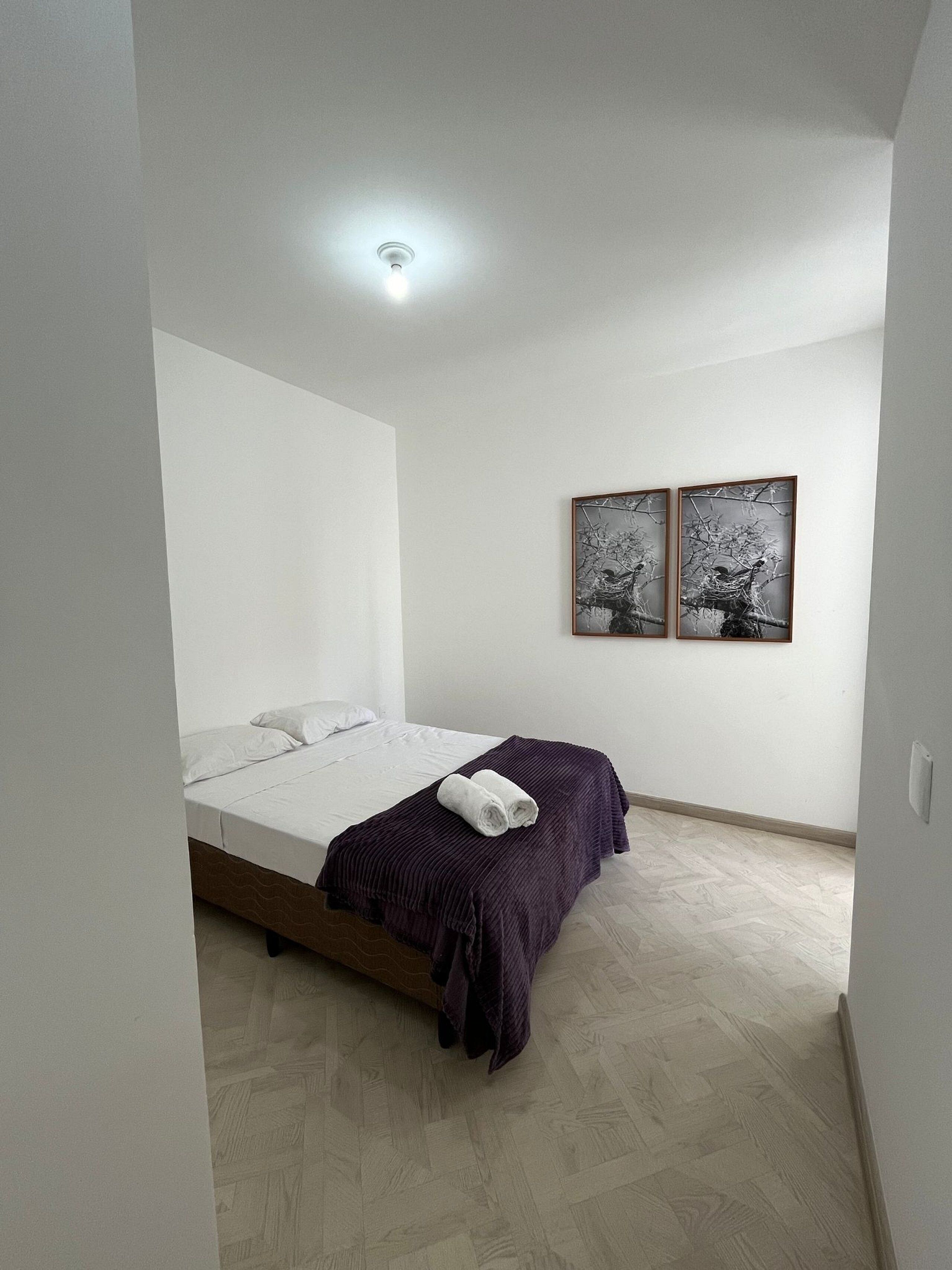 Un dormitorio con una cama, un edredón morado y dos cuadros colgados en la pared.