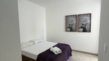 Un dormitorio con una cama, un edredón morado y dos cuadros colgados en la pared.