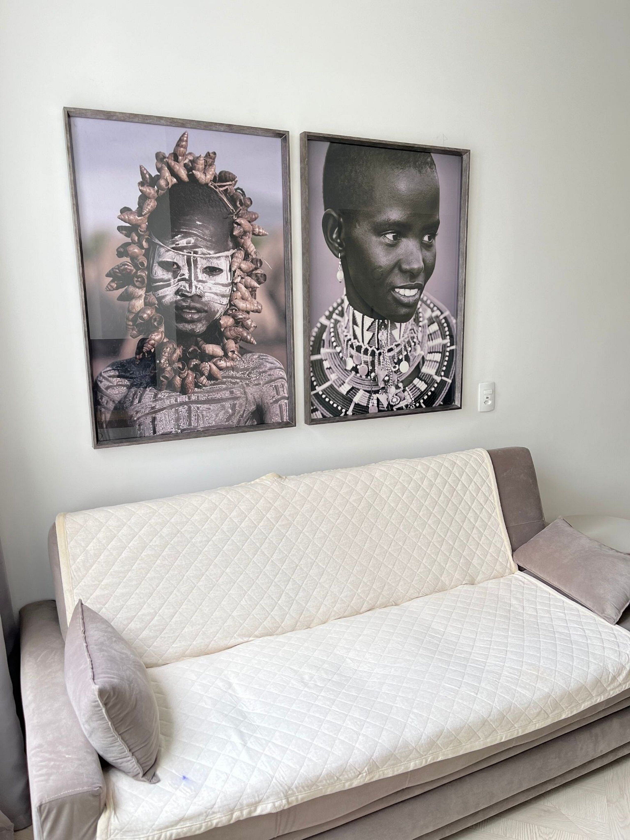 A sofa with a quilted cover and two pillows, a wall with two framed photographs, and a light switch.