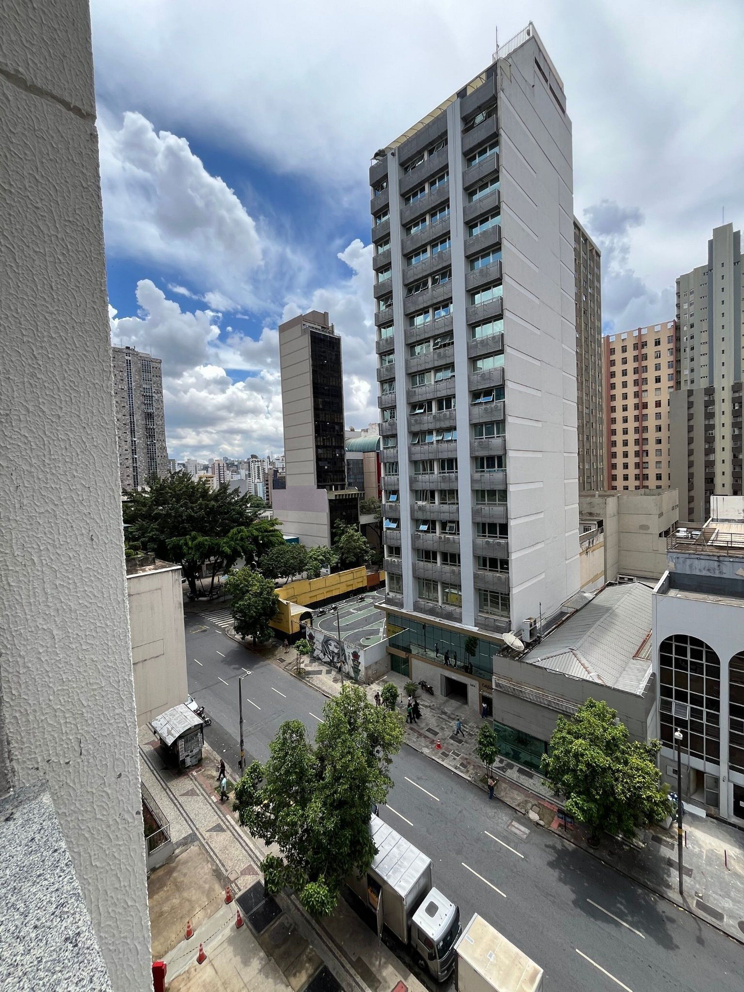 Un edificio alto con varios pisos, una calle con vehículos y un cielo despejado.