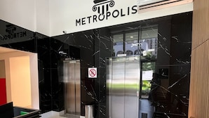 Ett modernt entréområde med en skylt som visar texten ”METROPOLIS”, en papperskorg, en hiss och en sittgrupp med stolar.