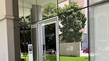 A modern building entrance with a glass door, a number '1203' sign, and a small outdoor area with plants.