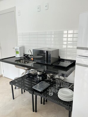 A kitchen with a microwave, coffee maker, and a coffee pot on a black countertop. - LK Centro 3 (Belo Horizonte)