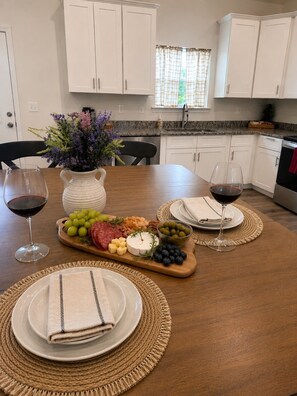 A dining table set with plates, a wooden board with cheese and grapes, two wine glasses, and a vase with flowers. - Lookout Retreat  Near Chattanooga (Trenton)