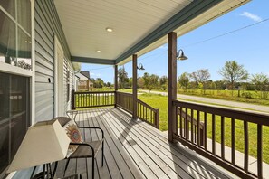 A covered porch with a table and chairs, a lamp, and a view of a road and greenery. - Lookout Retreat  Near Chattanooga (Trenton)