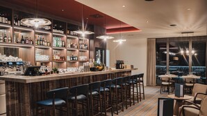 A bar area with a long counter, multiple stools, and a variety of bottles and glasses. - Guerneres Resort & Spa (Grimentz)