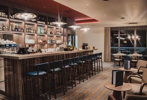 A bar area with a long counter, multiple stools, and a variety of bottles and glasses.
