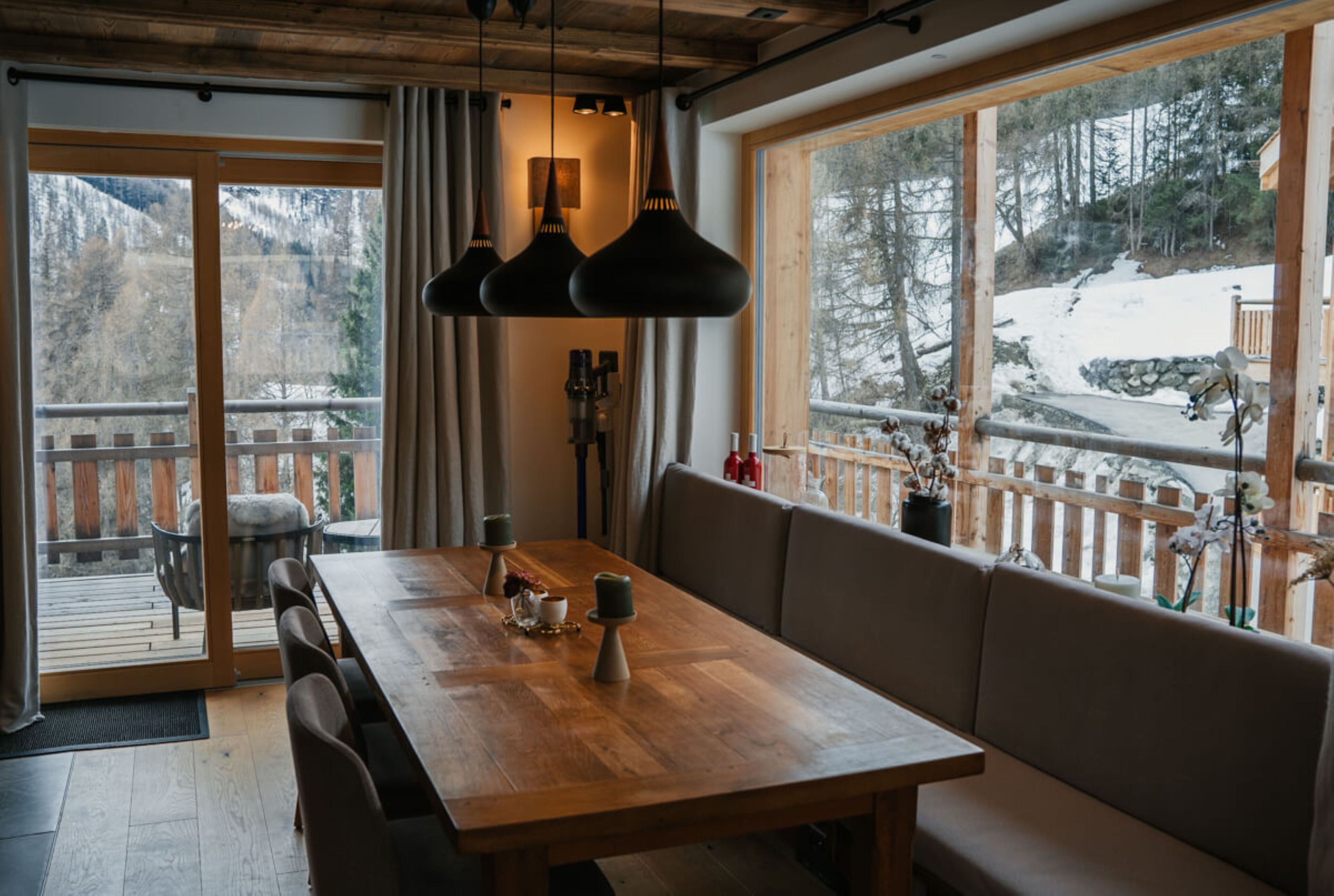 A wooden dining table with chairs and a bench, a fireplace, and a view of a snowy landscape through large windows.
