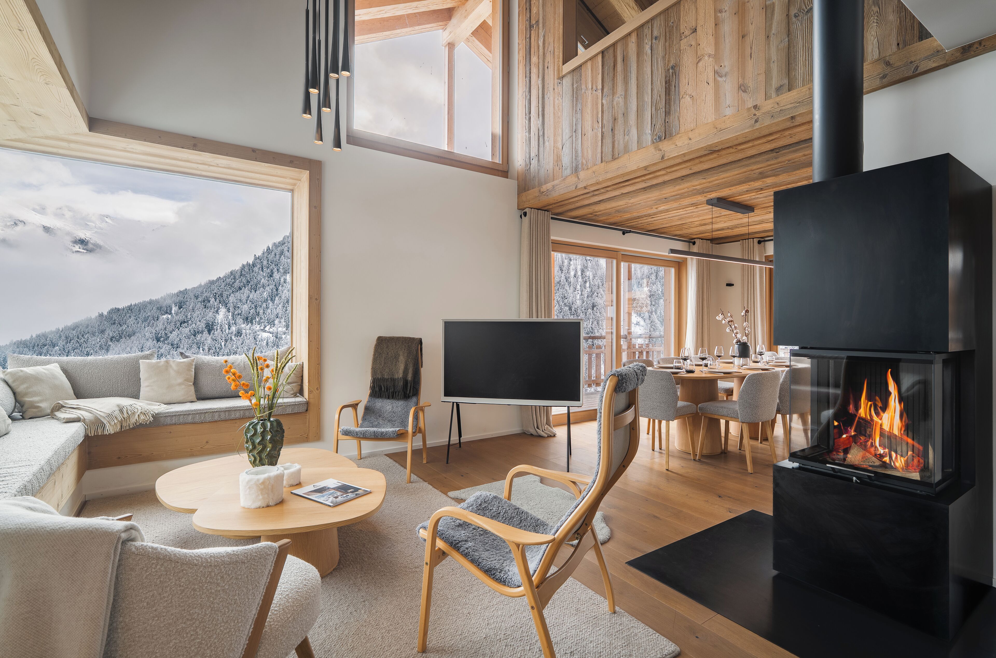 A modern living room with a fireplace, a sofa, a dining area, and a large window overlooking a snowy landscape.