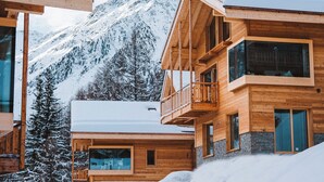 A wooden chalet with a balcony, large windows, and a view of snow-covered mountains. - Guerneres Resort & Spa (Grimentz)