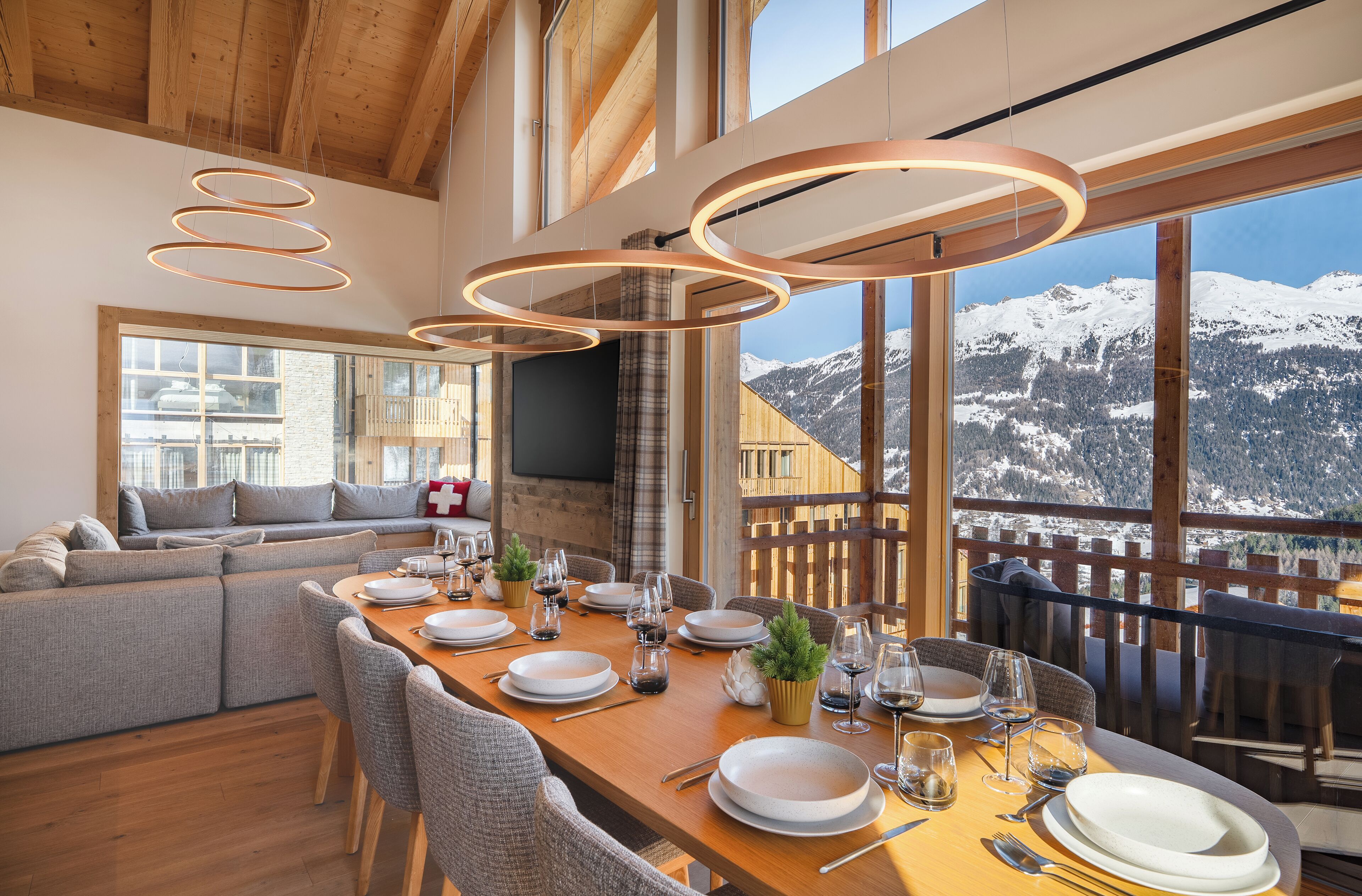 A dining area with a wooden table set for four, large windows offering a mountain view, and a cozy seating area with a sofa.