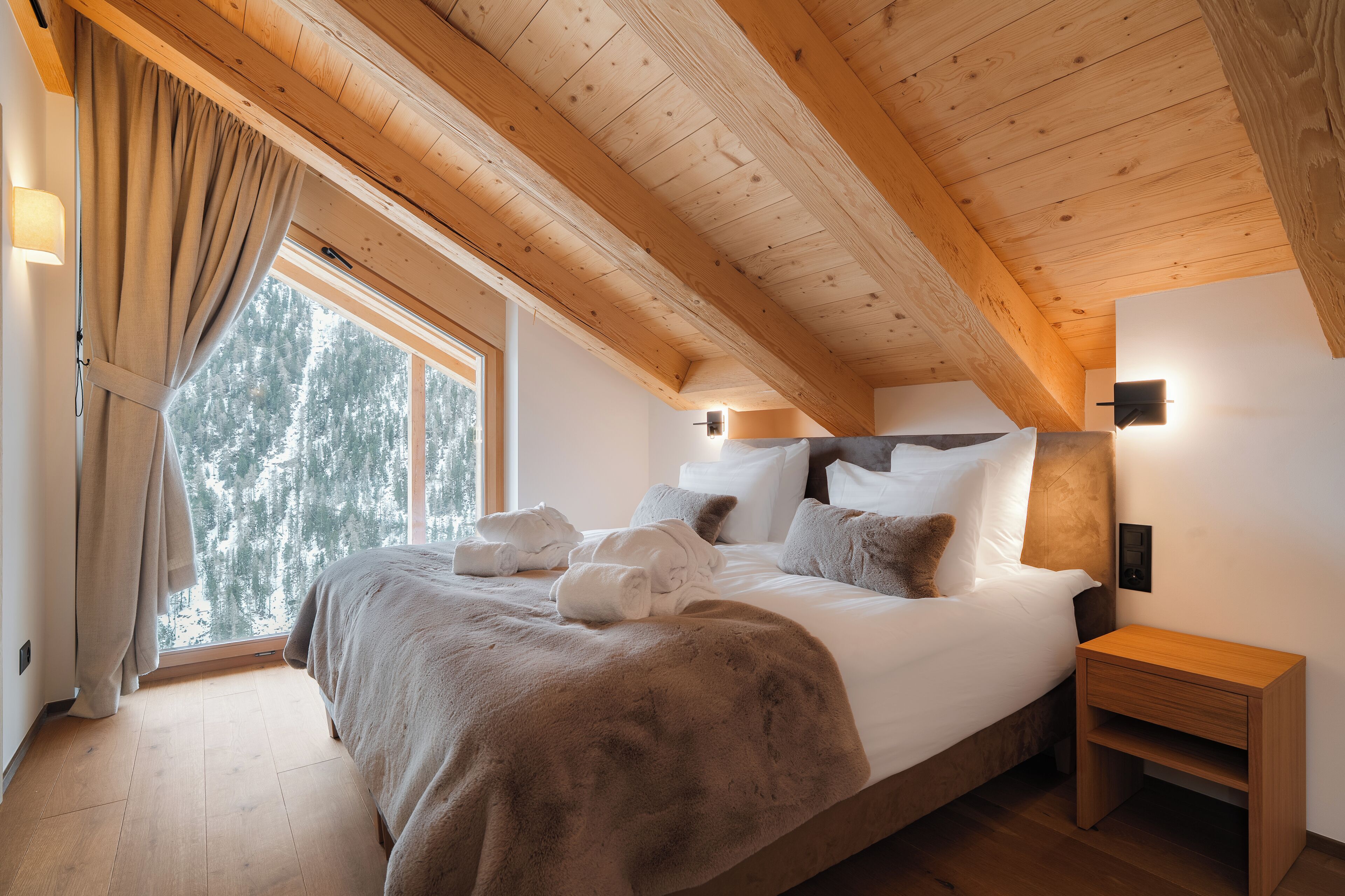 Une chambre à coucher avec un plafond en bois, un grand lit avec une literie blanche, une table de chevet et une fenêtre avec des rideaux.
