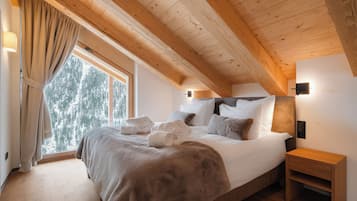 Una camera da letto con soffitto in legno, un letto grande con biancheria bianca, un comodino e una finestra con tende.