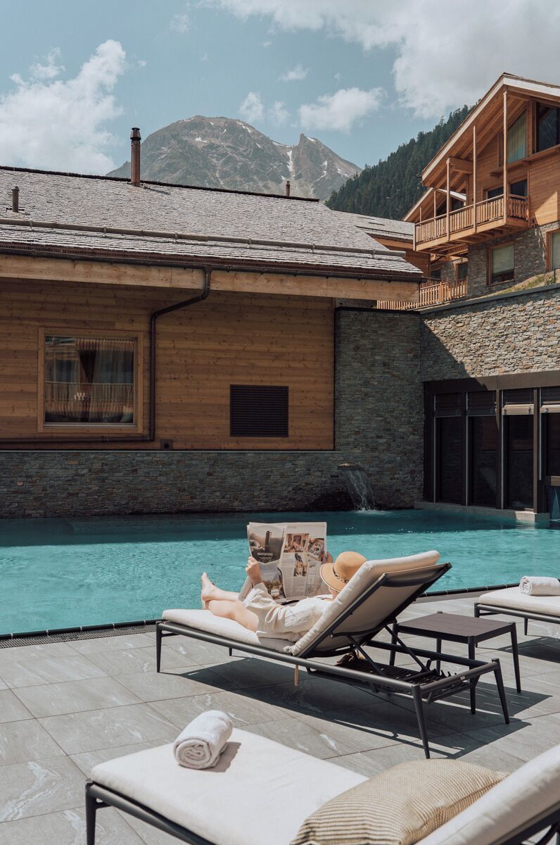 A poolside area with lounge chairs, a wooden building, and a mountain backdrop.
