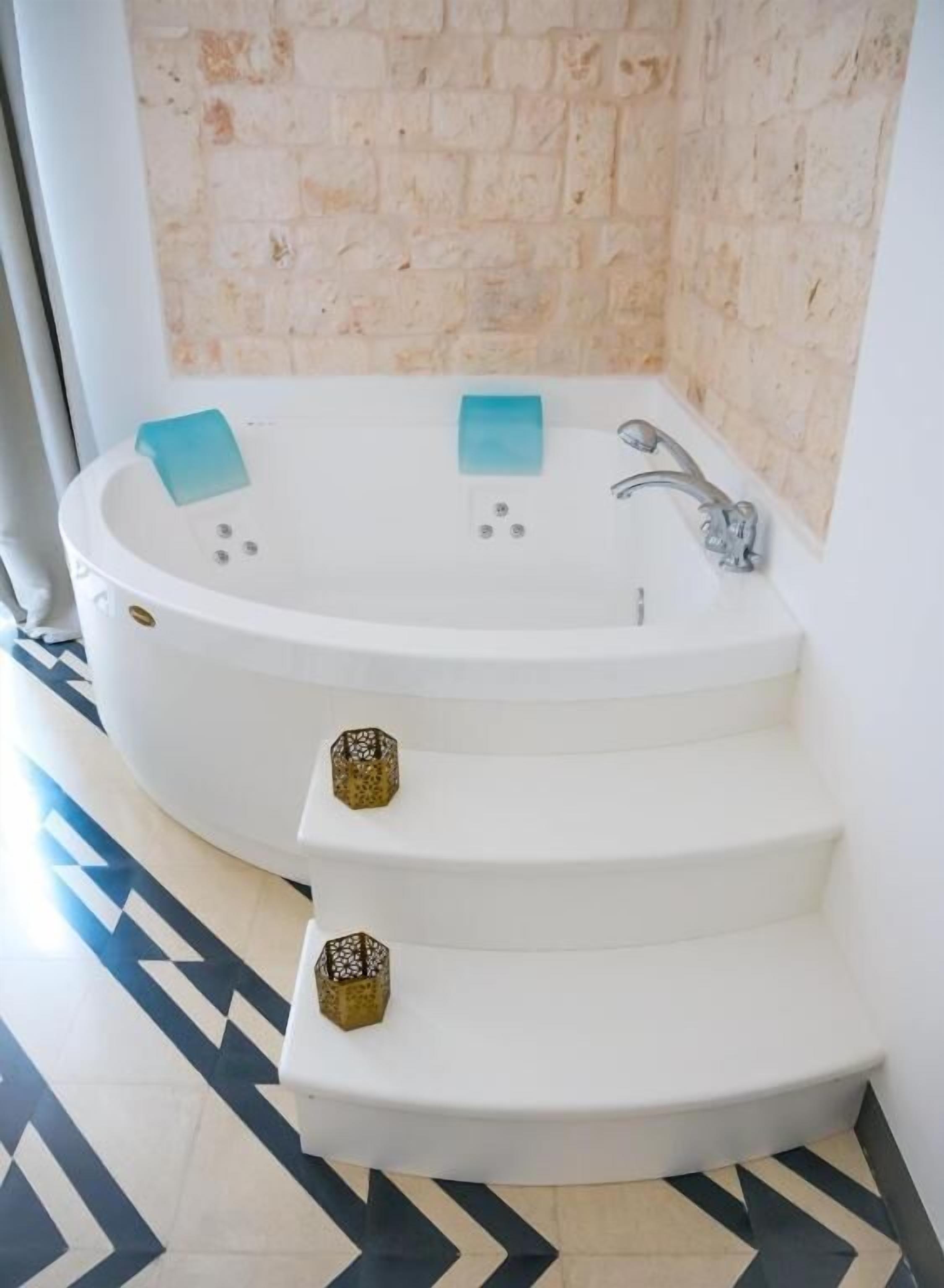 A modern bathroom with a freestanding bathtub, two steps leading up to it, and a patterned floor.