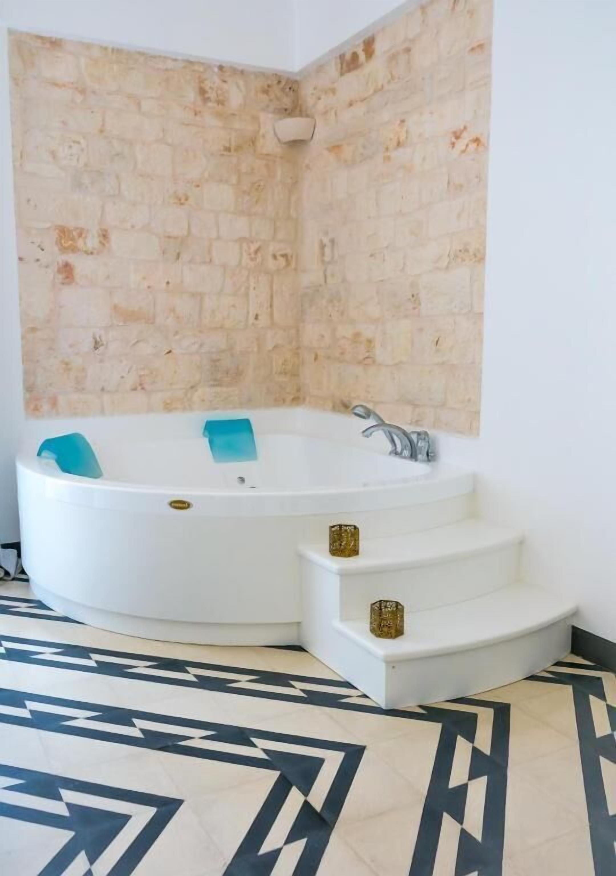 A corner bathroom with a white bathtub, a tiled wall, and a patterned floor.