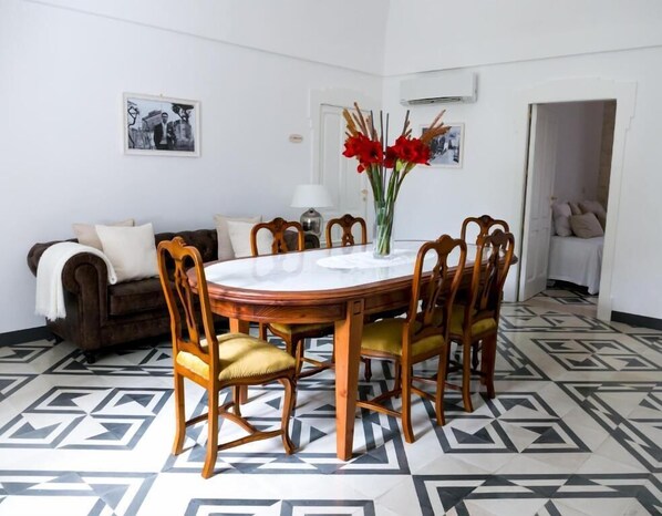 A dining area with a round table, chairs, a vase with red flowers, and a patterned floor.
