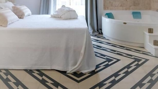 A hotel room with a bed, a chandelier, a bathtub, and a patterned floor. - Villa Aurelia (Locorotondo)