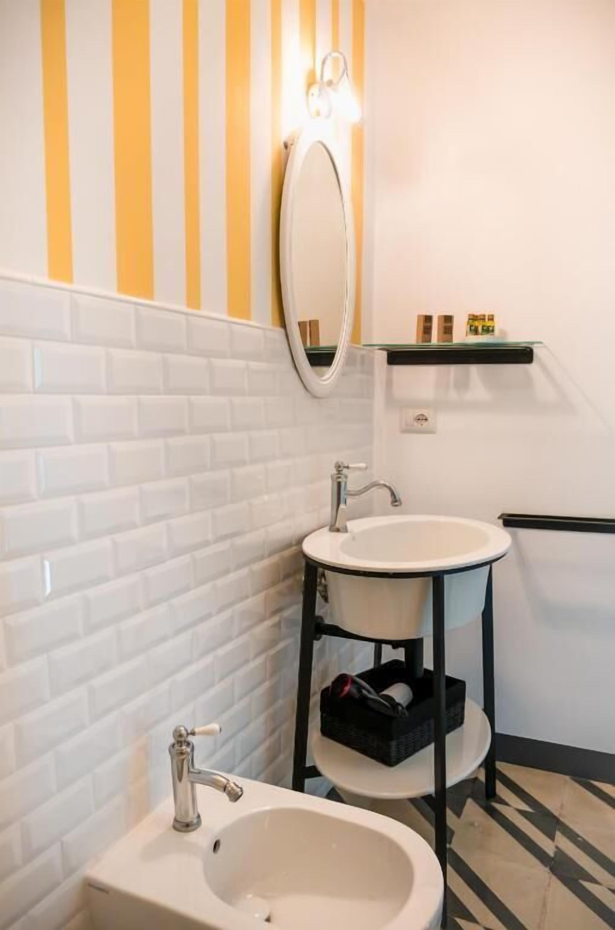 A bathroom with white tiled walls, a white sink, a mirror, and a striped wall decoration.