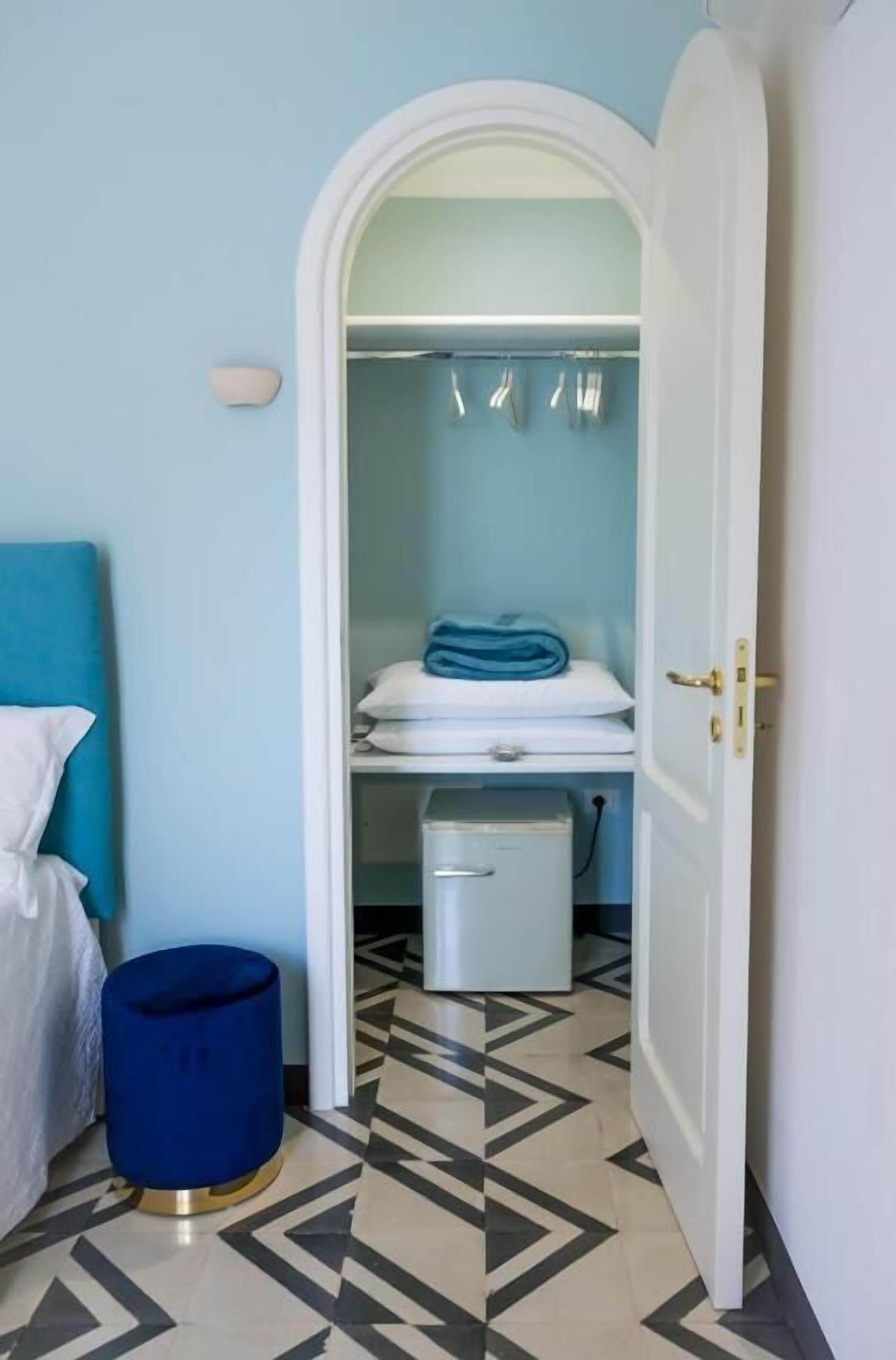 A hotel room with a bed, a blue trash bin, a white wardrobe, and a tiled floor.
