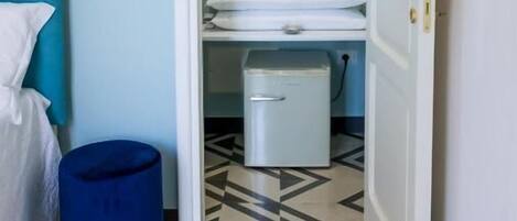 A hotel room with a bed, a blue trash bin, a white wardrobe, and a tiled floor.
