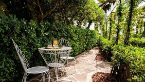 A stone patio with a round table and chairs, surrounded by lush greenery. - Villa Aurelia (Locorotondo)